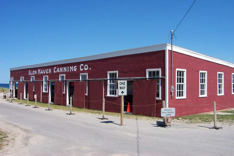 Red Glen Haven Canning Co. building with white-trimmed windows and open sliding doors beside Lake Michigan.