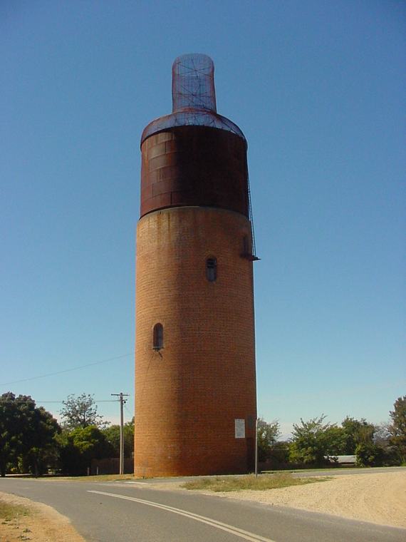 A roadside view shows the brick cylindrical tower, dark tank and narrow open mesh neck against a blue sky.