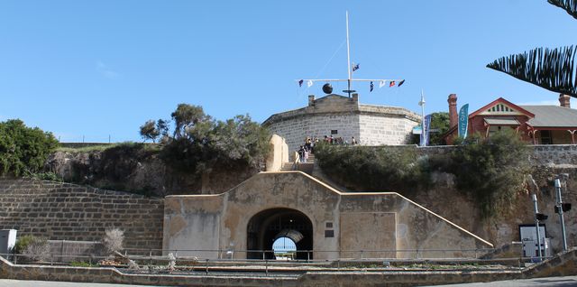 A limestone building stands above a broad stairway and arched tunnel entrance, with railway tracks crossing the foreground.