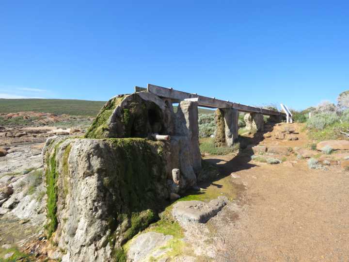 Mineral-encrusted wheel supports fill the foreground, with the wooden flume receding over stone piers.