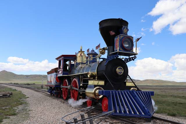 Blue, red and gold Jupiter replica with a broad black smokestack, red wheels and striped front pilot on railway tracks.