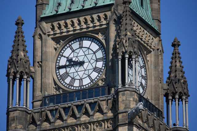 Two clock faces and carved stone details near the top of the Peace Tower.