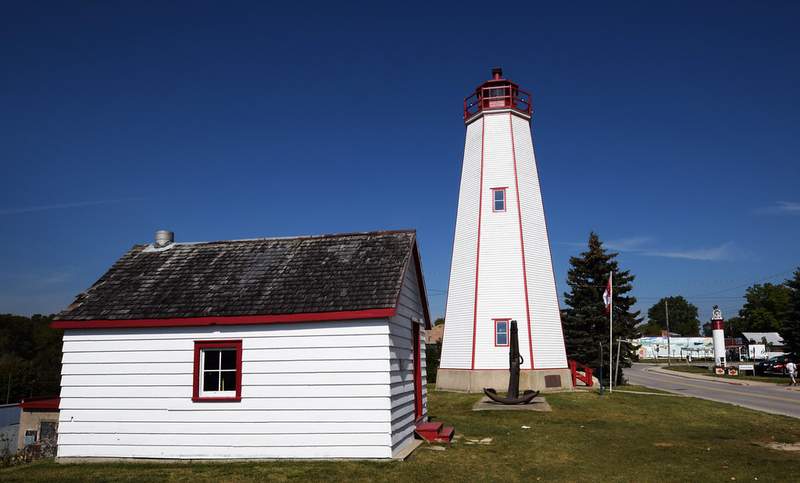 White tapered wooden lighthouse with red trim beside a low white building in Port Burwell.