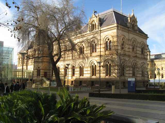 The stone library building faces a courtyard, with tall arched windows, steep roofs and small figures near its entrance.