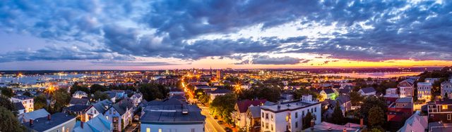 A broad stitched view from the Observatory shows city rooftops between two areas of water under an evening sky.