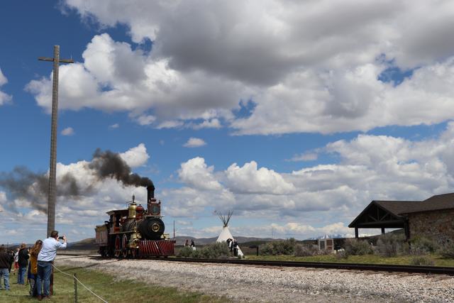 Red and black No. 119 replica emits dark smoke on railway tracks while small visitors watch from the side.