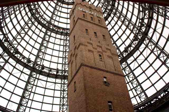Two faces of a tall brick tower, with Lead Pipe and Shot Factory wording near its battlements, surrounded by glass-roof framing.