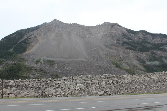 A broad bare mountain scar rises above a field of rocks and a road.