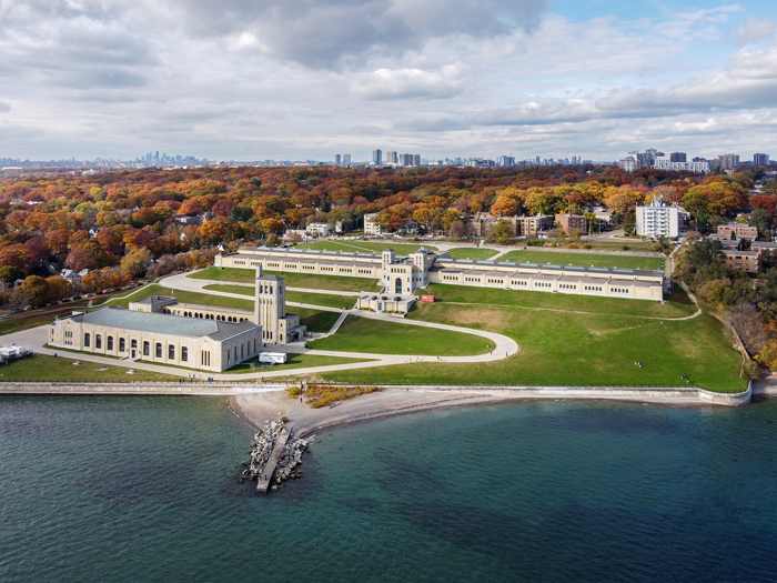 An elevated view across Lake Ontario shows the water-treatment buildings, long filter-building wings, terraces and lawns, with a wooded neighbourhood behind.