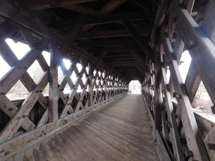 Wooden walking surface receding between intersecting timber walls beneath a covered roof.