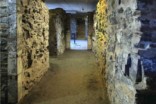 A passage runs between thick stone walls beneath a low modern ceiling.