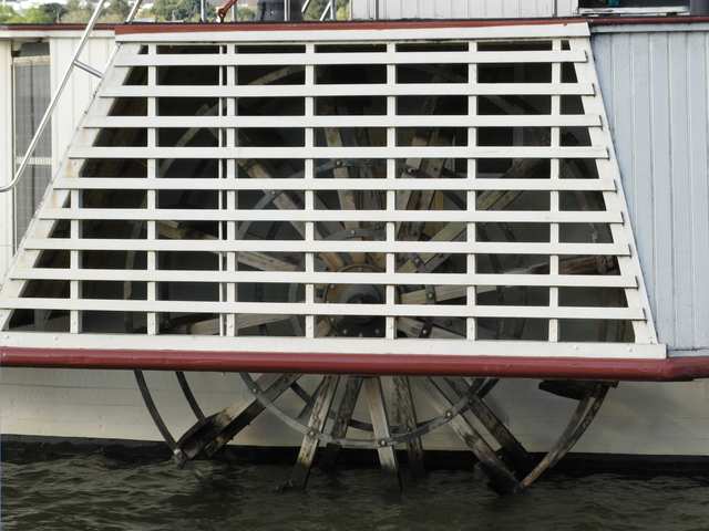 The wooden paddle wheel and metal braces are visible behind the slatted protective housing and at the waterline.