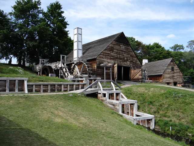 Timber mill buildings with large wooden waterwheels, channels and grass beside them.