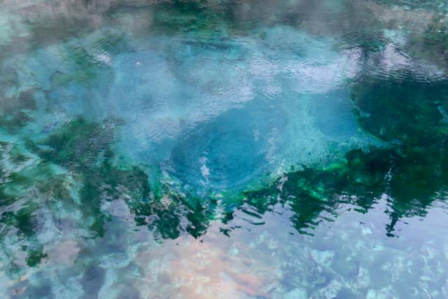 Ripples and reflections cross blue-green water above pale submerged rock.