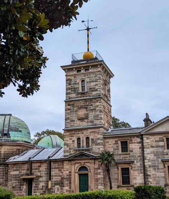 The yellow time ball rests near the foot of its mast above the sandstone tower, with domes below.