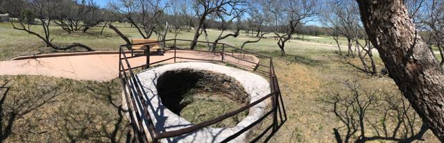 A wide panorama shows the circular kiln behind a metal railing, with a path, bench and trees around it.