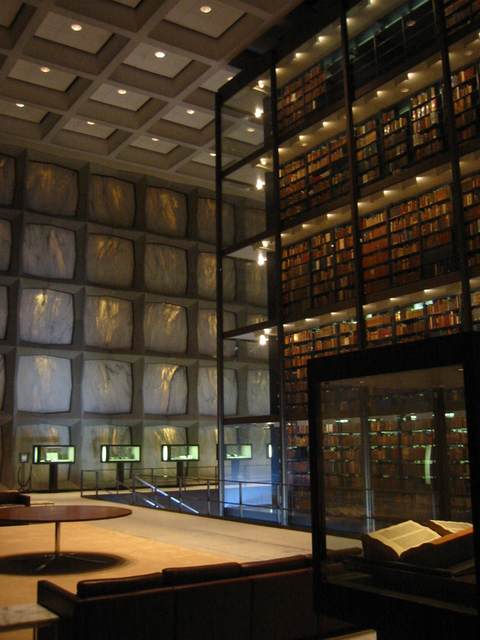 Warm light passes through marble panels beside a tall glass enclosure filled with shelves of books.