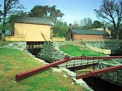 The tall wooden Great Gate housing stands over the canal at left, beside a lock chamber, brick gatehouse and stone walls.