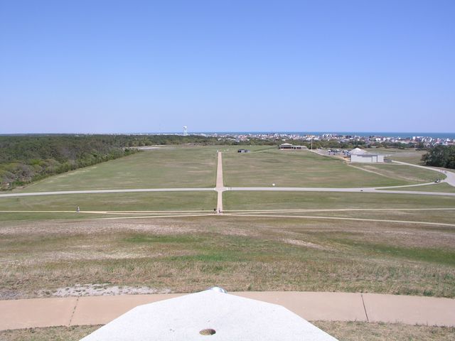 Grassed slopes and intersecting paths lead toward the memorial grounds, with distant buildings and trees.
