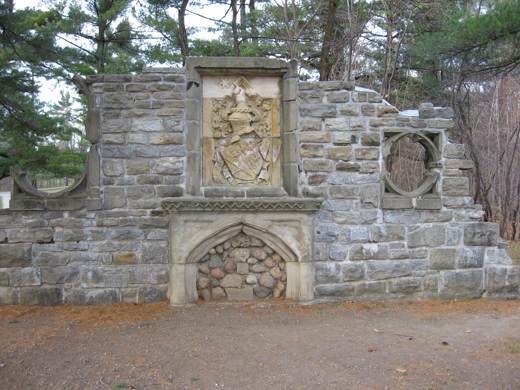 A freestanding stone wall with an arched fireplace opening, carved crest and decorative window openings.