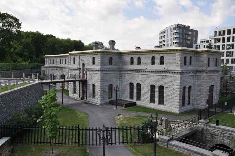 A long, low stone pumping station with arched windows, railings and paths, backed by modern buildings.