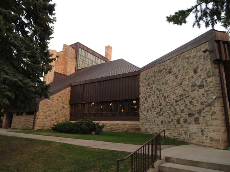 The modern church has a low sloping roof, broad windows, angular stone walls and a taller glazed section behind.