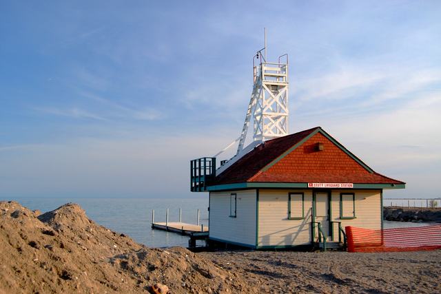 The white lifeguard station and rooftop lookout stand beside the lake, with earth piles and orange mesh in the foreground.