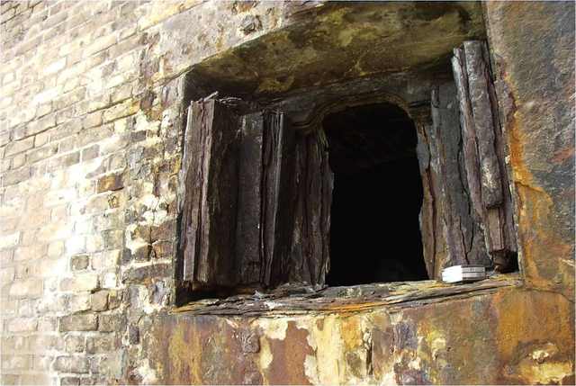 Layers of corroded iron surround a dark square opening in a brick wall.