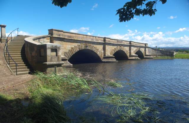 Three sandstone arches span the river beside a curving stairway.