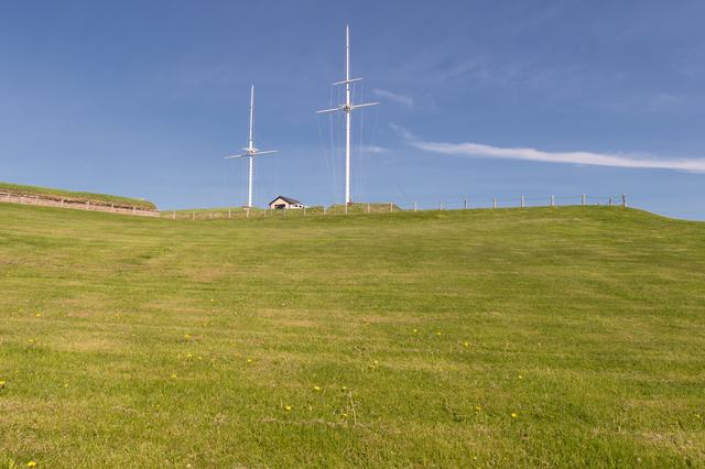 Two white signal masts and their rigging rise above grassy ramparts under a blue sky.