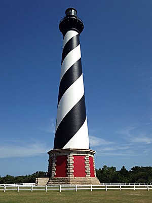The black-and-white spiral lighthouse rises above its red base and a white fence.