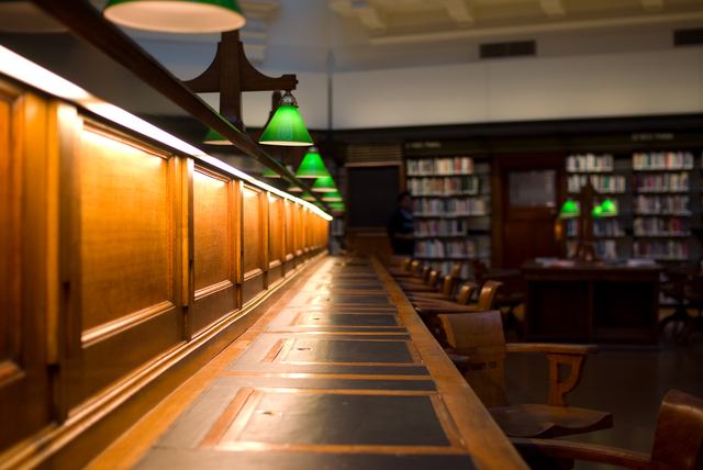 Wooden writing surfaces and chairs run beside a row of green lamps.