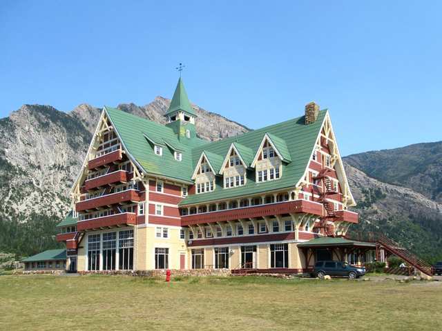 The hotel’s gabled tower, balconies and side wing seen across a grassy slope, with mountains behind.
