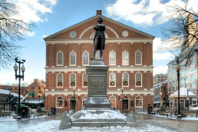 The brick façade of Faneuil Hall behind a large statue of Samuel Adams, with snow around the pedestal and plaza.