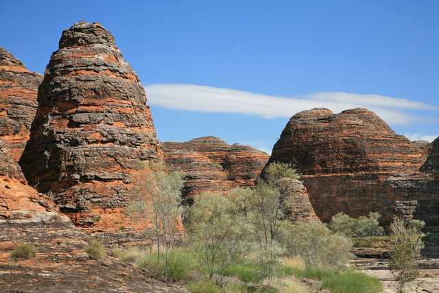 A tall banded sandstone dome at left and lower rounded domes at right, with scrub in the foreground.