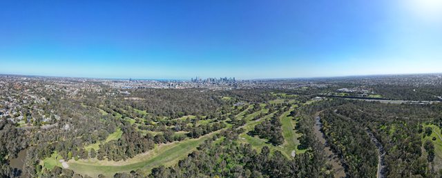 An aerial panorama shows river bends and a wooded park amid Melbourne’s urban area.