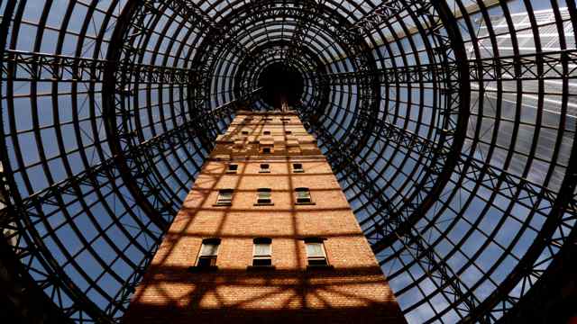 Looking steeply upward along a brick tower into the concentric steel framing and glass of a large conical roof.