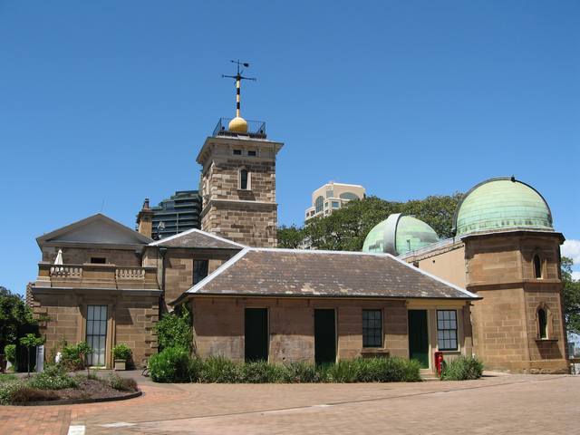 Sydney Observatory’s sandstone buildings and green domes, with a yellow time ball atop the central tower.
