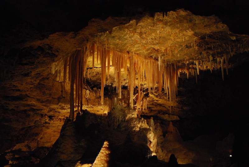 Amber-lit stalactites hang from a dark cave roof above irregular rock formations.