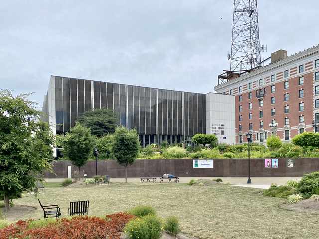 The signed Buffalo and Erie County Public Library building beyond planted beds and benches, with neighbouring buildings to the right.