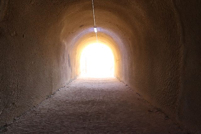 An arched, rough-walled passage with an overhead light leads towards an intensely bright opening.