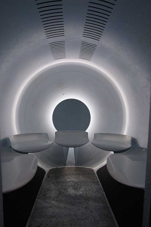 Five molded seats arranged inside a rounded white tram capsule, seen through its open entrance.