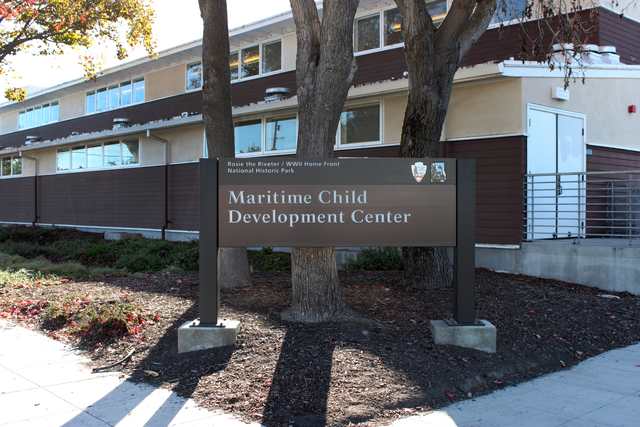 A sign identifying the Maritime Child Development Center stands before a low, two-story building shaded by a tree.