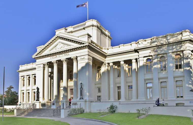 The pale front of St Kilda City Hall has a columned portico, triangular pediment, broad steps and an Australian flag above it.
