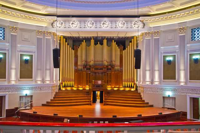 The organ stands above the empty auditorium stage, framed by columns and a decorative relief band.