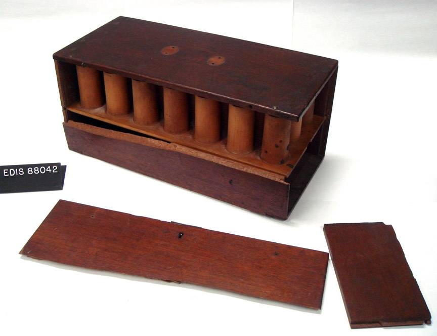 A dark wooden case with cylindrical compartments, two detached wooden panels and an EDIS 88042 catalogue label.