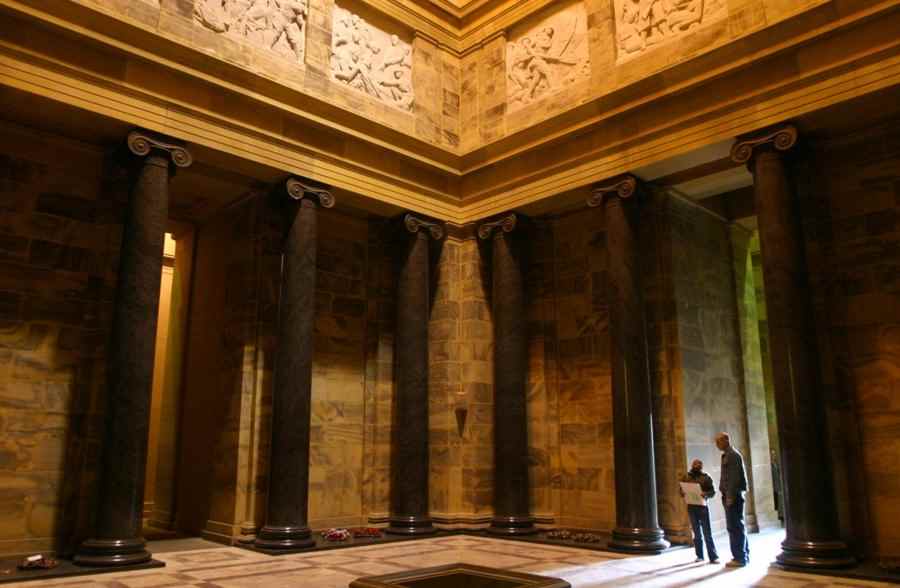 Stone columns and a fixed sculptural frieze inside the Sanctuary, with two visitors near a doorway.