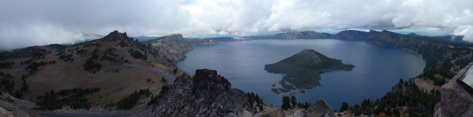 Wide overcast panorama of Crater Lake, Wizard Island and the surrounding caldera walls.