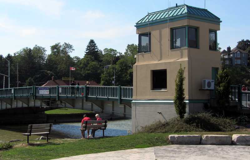 Close view of the lift bridge control building, a closed lifting leaf and benches beside the creek.