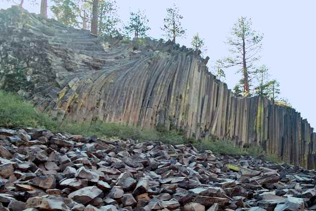 Long vertical and curved rock columns rise above a slope of fallen angular stones.